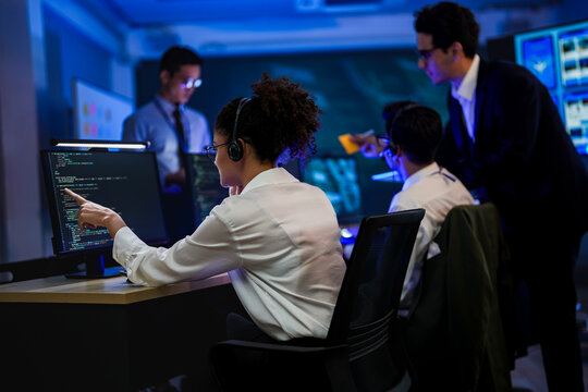Professional female programmer typing code on computer in cyber security control room. IT software engineer wearing headset analyzing network data in modern blue light office.