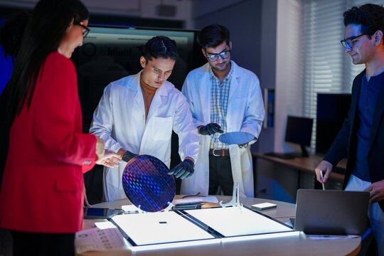 Professional researchers in lab coats discussing science project with business team. Tech engineers analyzing electronic components in modern night shift laboratory.