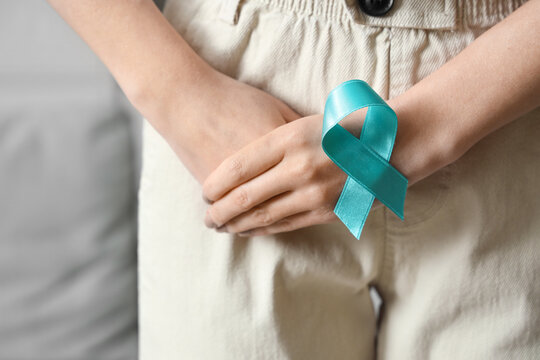 Young woman with turquoise ribbon at home, closeup. Cervical Health Awareness Month