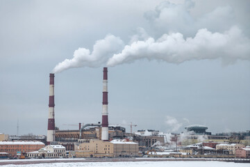 A winter scene shows a power plant in Saint Petersburg with white smoke coming out of two striped red and white smokestacks. The buildings are covered in snow.
