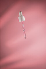 Dropper dispensing a single drop of clear cosmetic serum, highlighting skincare, beauty, and wellness concepts against a soft pink backdrop with subtle shadows