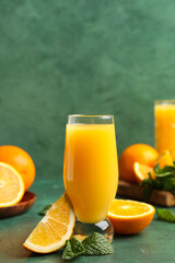 Glass of tasty juice with oranges and mint leaves on green grunge background