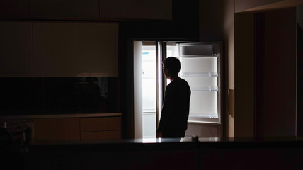 机とキッチンの光の前に立つ人物シルエット