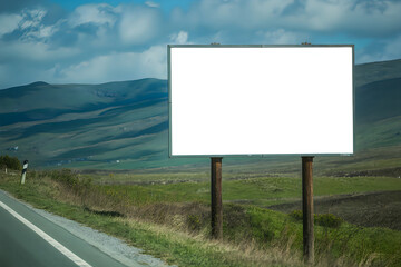 Blank billboard on a grassy roadside with rolling hills background white empty