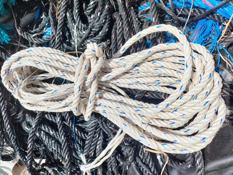 Close-up of a coiled white nylon rope with blue tracer. Detailed texture of industrial cordage for maritime, shipping, logistics, construction, and heavy-duty utility concepts.
