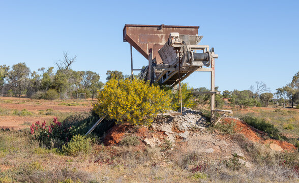 A heavy duty conveyor system for processing opal bearing ore but now scrapped and half hidden by pioneer plants growing in the exposed soil in the semi-arid country at Yowah in Queensland, Australia.