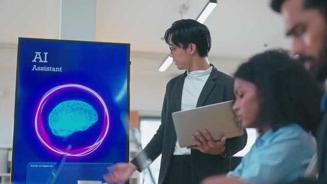 Asian man present work to team interacting with AI voice technology on screen, waiting and listening to audio feedback in a modern office.