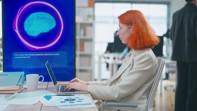 Businesswoman in modern office working on laptop and using smartphone voice recognition with AI assistant technology to enhance communication, multitasking, and productivity.