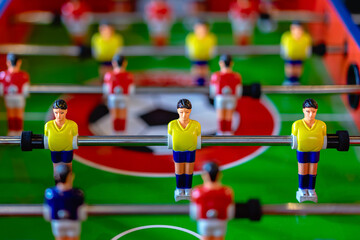 Classic colorful foosball table with red and yellow players. Beautiful indoor recreation and table soccer competition background. Table football game with selective focus on miniature soccer players