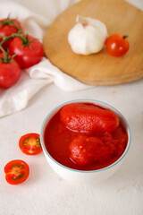 Bowl of canned tomatoes and garlic on light background
