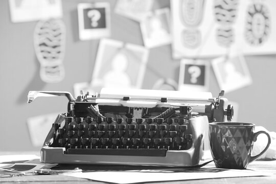 Retro typewriter and cup of tea on table against crime board