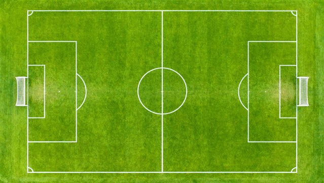 an aerial view of a rectangular soccer field with a vibrant green grass surface. The field is symmetrically divided by a white center line,