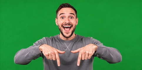 Excited man pointing down with both hands and wide smile on a green screen background, promoting something below.