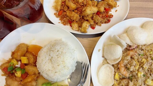 Three Asian dishes are served on a table, including rice, sweet‑sour meat, shrimp fried rice, and spicy fried bites, paired with two glasses of iced tea.