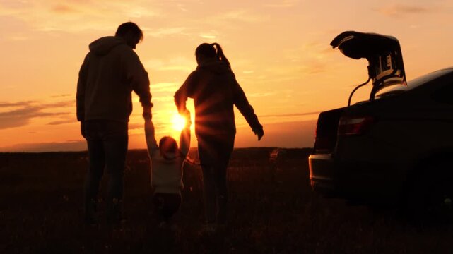 Silhouettes of having fun mom dad kid. Golden sunset, cheerful joyful family at holidays holding hands, lifting baby girl high in air, playing together. Fun active game. Traveling by car to nature.