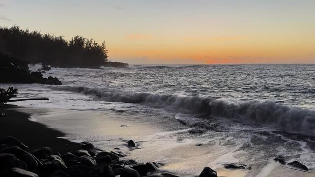 Waves crashing at Kehena Beach with distant fisherman silhouette.