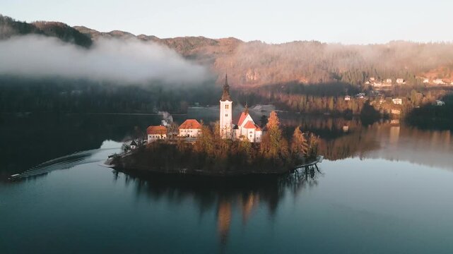 A gentle aerial movement advances away and upwards from the tranquil church island that Sts in the middle of the magnificent lake bled in Slovenia, Central Europe.