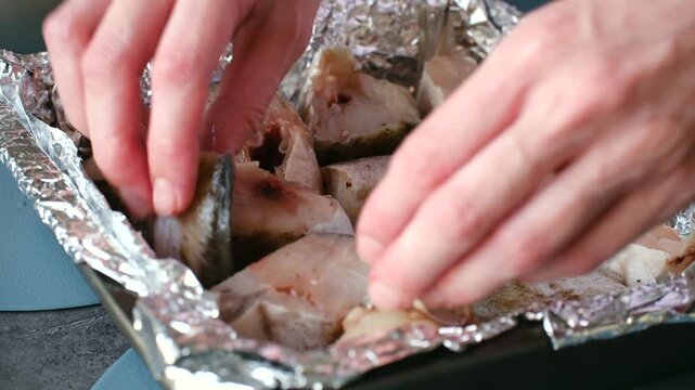 Professional chef preparing healthy seafood dish by carefully arranging seasoned raw fish fillets on baking sheet lined with aluminum foil, getting them ready for cooking in oven