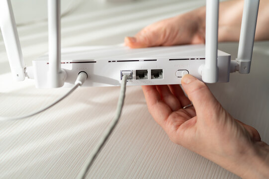 Hand of a Person Pressing a Reset Button on the Back of a White WiFi Router with Ethernet Cables