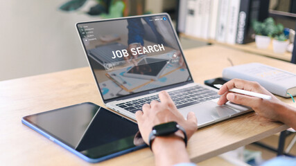 Close up of professional searching jobs online on digital tablet at modern office desk with laptop and planner. Job search, career opportunity, recruitment and employment concept in digital age.