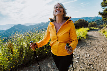 Active senior woman hiking on outdoor trail using trekking poles © oneinchpunch