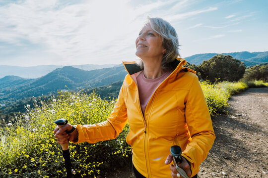 Active senior woman hiking on outdoor trail using trekking poles