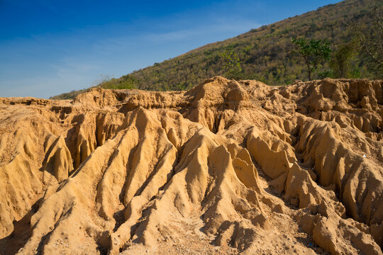 A unique rock landscape featuring deep canyons carved by geological processes, set against a backdrop of mountains and a clear blue sky. This terrain is formed in arid regions through erosion, rainfal