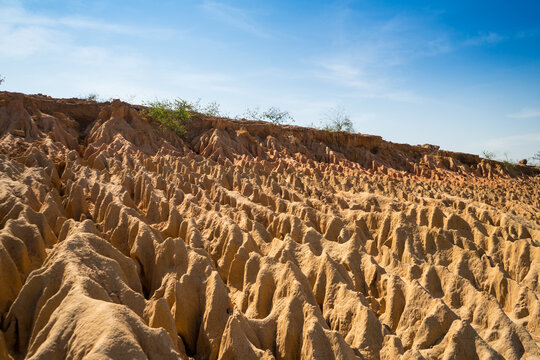A unique rock landscape featuring deep canyons carved by geological processes, set against a backdrop of mountains and a clear blue sky. This terrain is formed in arid regions through erosion, rainfal