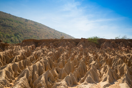 A unique rock landscape featuring deep canyons carved by geological processes, set against a backdrop of mountains and a clear blue sky. This terrain is formed in arid regions through erosion, rainfal