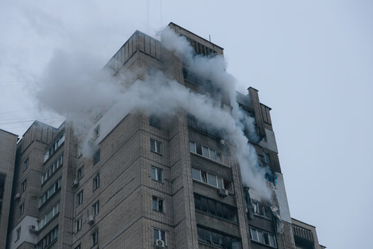 Dense smoke pours from a severely damaged high-rise apartment building. Shattered windows and destroyed balconies show the aftermath of a major fire or explosion.