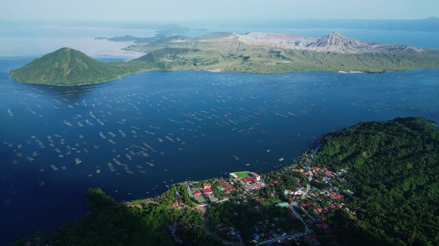 Daytime aerial view from Binintiang Malaki Western Viewpoint capturing Taal Volcano, crater, Taal Lake, Agoncillo Baywalk, and square fishponds with tiny boats in one panoramic frame.
