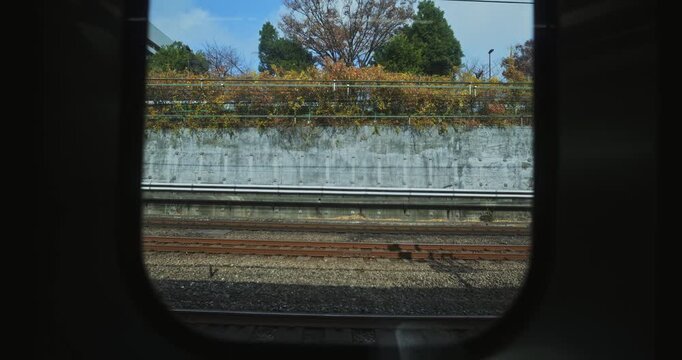 View outside of train window to tracks, autumn trees and Japanese buildings - wide