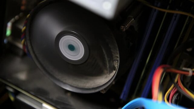 Spinning CPU cooler fan in computer case. Dust accumulation on blades. Power supply wires, data cables visible. Internal view of computer hardware, active cooling.