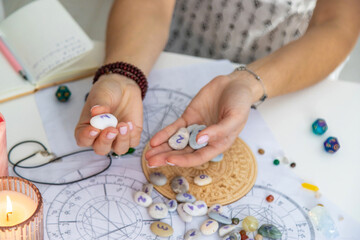 Astrologist hands holding numerology stones over natal charts and zodiac wheel