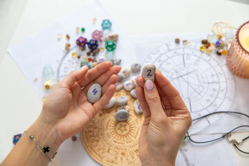 Astrologist hands holding numerology stones over natal charts and zodiac wheel