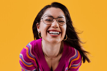 Happy young woman wearing glasses smiling against yellow background