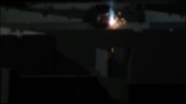 Bright sparks flash industrial process dark factory. Blurred structural elements hint workshop interior. Raw energy metalworking, fabrication, construction. Industrial activity; nobody present. Indoor