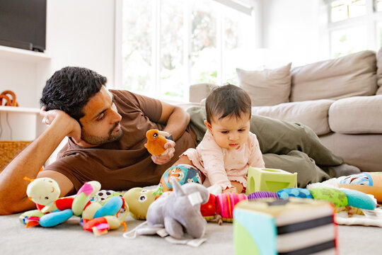 Indian dad playing with baby girl holding up colourful toy inside home