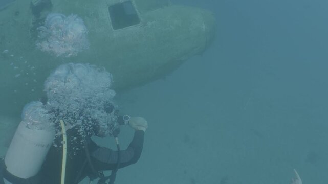 log footage of scuba divers  exploring an air craft wreck underwater. Ocean pollution. metal on ocean floor