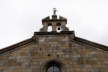 Stone church facade with bell tower and cross.. Parish Church of Our Lady of the Assumption in La Alberca, Salamanca, Spain