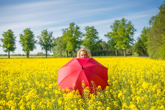 Mature woman with red umbrella standing amidst oilseed rapes against sky