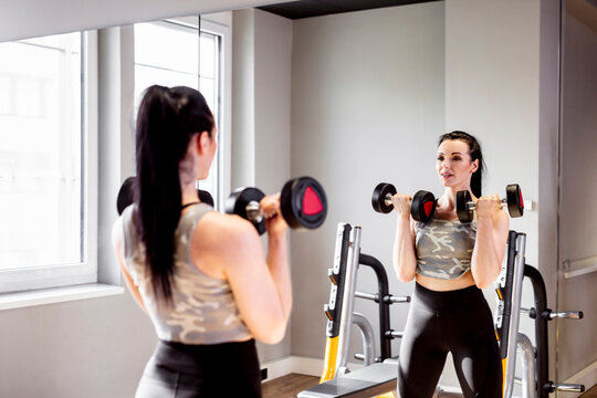 Woman lifting dumbbells in gym looking in mirror