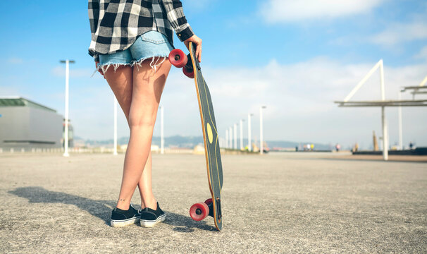 Back view of young woman with longboard in front of beach promenade, partial view