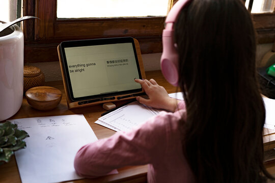 Girl wearing headphones translating languages on digital tablet while learning comics at home