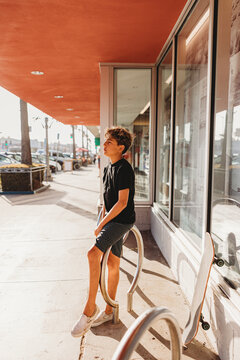 Boy standing a sidewalk next to his skateboard.