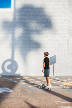 Boy skating in parking lot with white brick wall as the background.