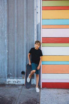 Boy leaning against a colorful wall with his skateboard.