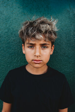 Portrait of a boy standing in front of a green concrete wall.