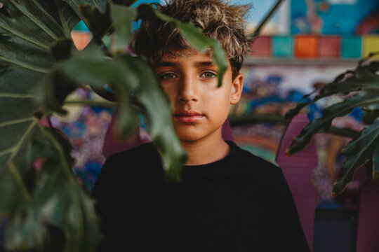 Serious boy standing behind a large green leaf.