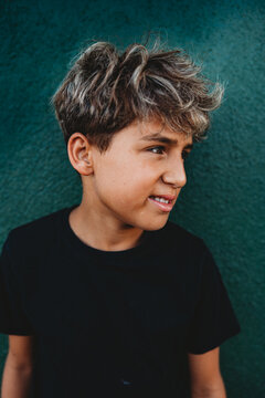 Boy with a smirk standing in front of a green concrete wall.